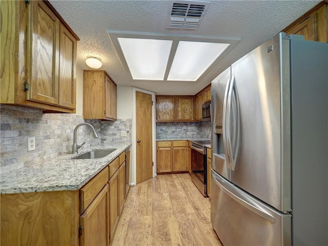 7140 Premont Dr Unit 12, Corpus Christi, TX 78414 - kitchen featuring appliances with stainless steel finishes, a sink, light wood finished floors, brown cabinetry, and decorative backsplash