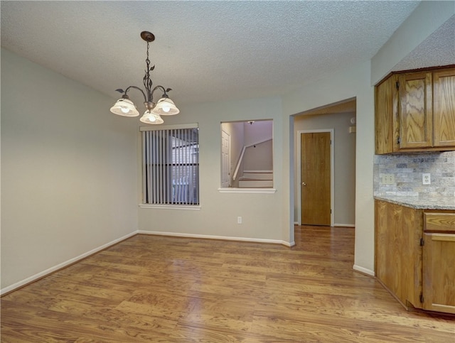 unfurnished dining area with light hardwood / wood-style flooring, a notable chandelier, and a textured ceiling