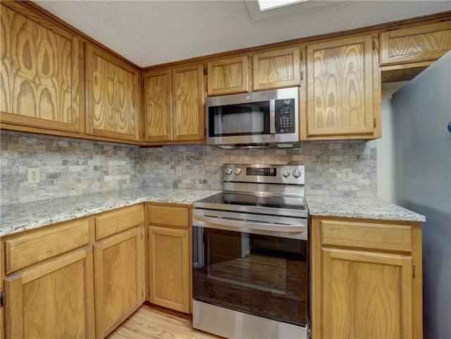 kitchen with light stone countertops, backsplash, a textured ceiling, stainless steel appliances, and light hardwood / wood-style flooring