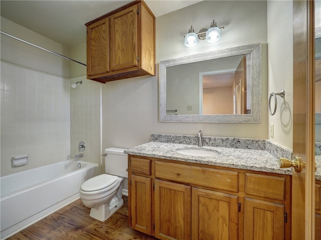 full bathroom with hardwood / wood-style floors, vanity, tiled shower / bath combo, and toilet