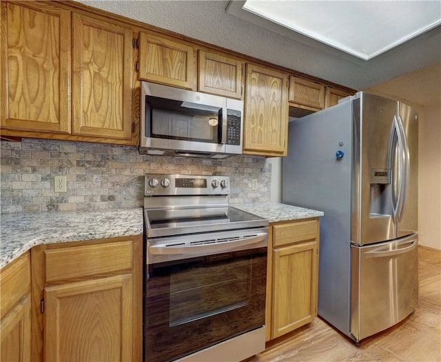 kitchen featuring decorative backsplash, appliances with stainless steel finishes, light stone counters, a textured ceiling, and light hardwood / wood-style floors