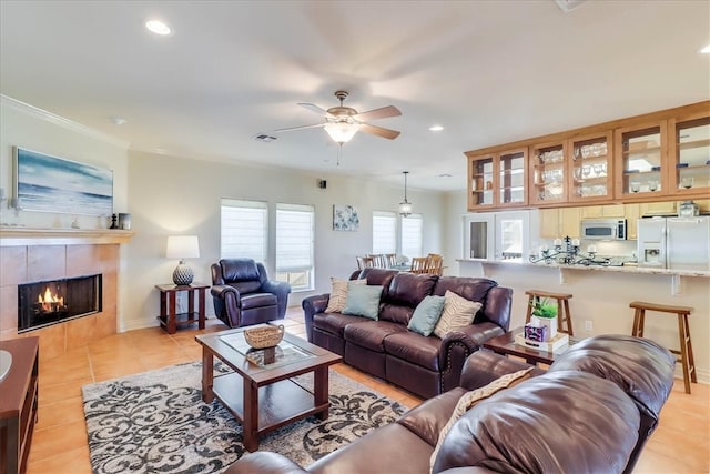 living room featuring a fireplace, ceiling fan, crown molding, and light tile patterned flooring