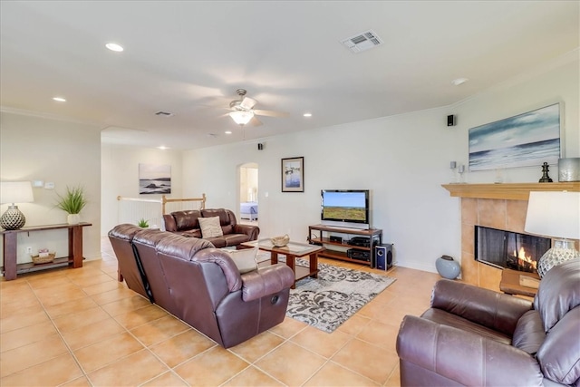 tiled living room with ceiling fan, crown molding, and a fireplace