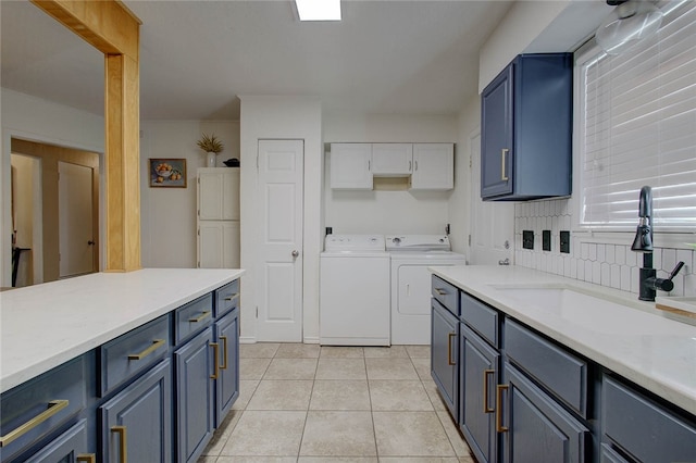 kitchen featuring blue cabinets, light tile patterned floors, sink, washing machine and clothes dryer, and backsplash