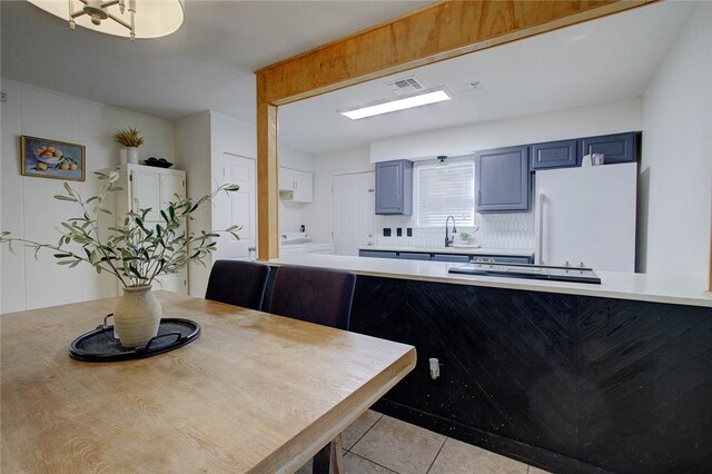 kitchen with light tile patterned flooring, kitchen peninsula, decorative backsplash, and white fridge