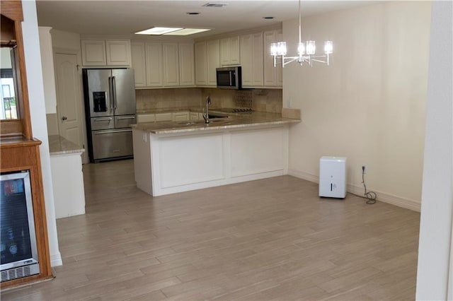 kitchen with beverage cooler, light wood finished floors, appliances with stainless steel finishes, and backsplash