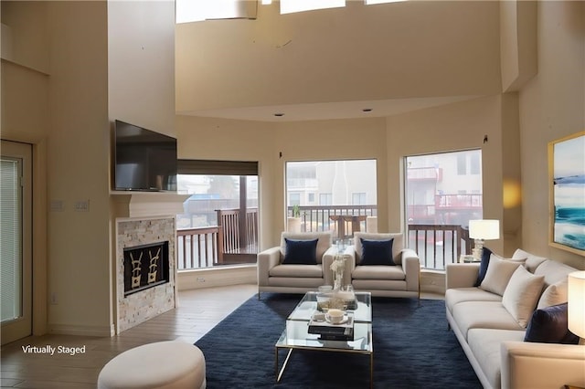 living area featuring a stone fireplace, a towering ceiling, and wood finished floors