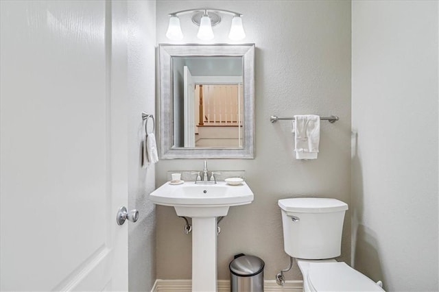 half bath with toilet, baseboards, and a sink