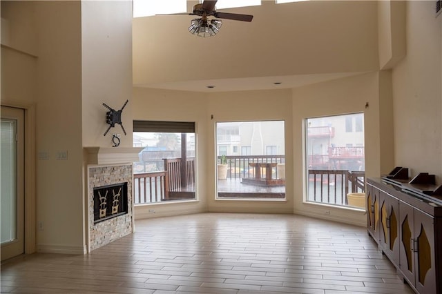 unfurnished living room featuring wood finished floors, a fireplace, a towering ceiling, and ceiling fan