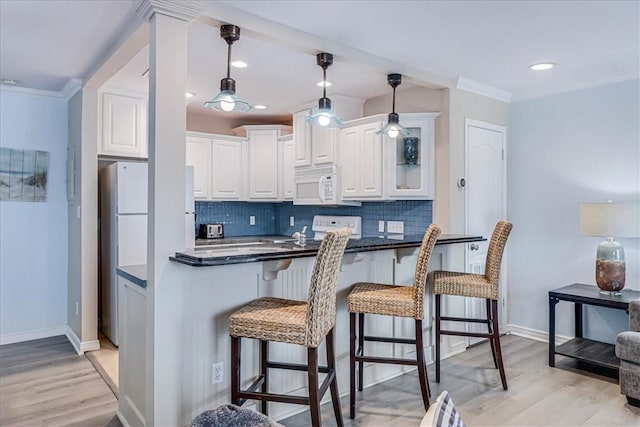 kitchen featuring white appliances, white cabinets, a kitchen breakfast bar, tasteful backsplash, and dark countertops