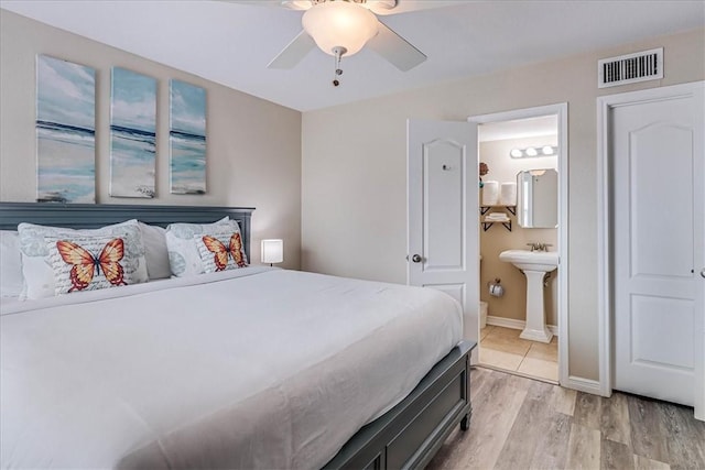 bedroom featuring baseboards, visible vents, connected bathroom, light wood-style floors, and a sink