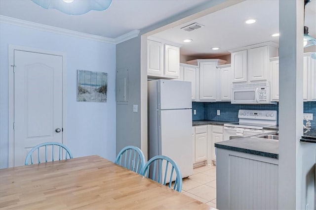 kitchen with light tile patterned floors, dark countertops, ornamental molding, white cabinets, and white appliances