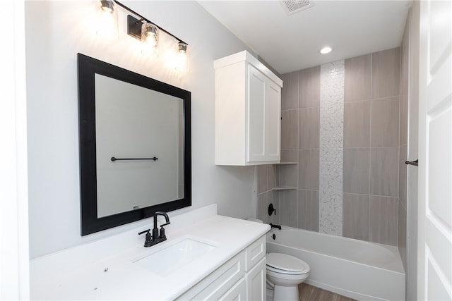 full bathroom with hardwood / wood-style flooring, vanity, tiled shower / bath combo, and toilet