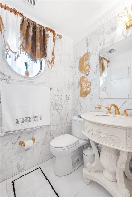 half bath featuring visible vents, toilet, marble finish floor, tile walls, and crown molding