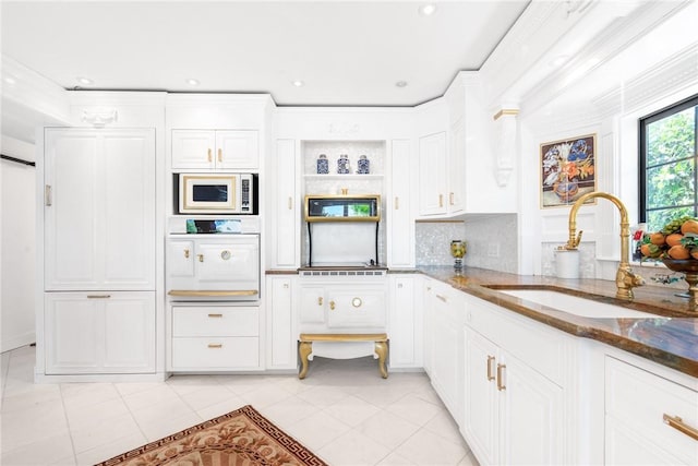 kitchen with white microwave, backsplash, dark stone counters, white cabinetry, and a sink