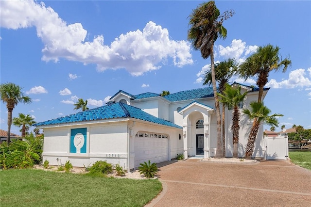 mediterranean / spanish-style house with a tiled roof, concrete driveway, stucco siding, an attached garage, and a gate