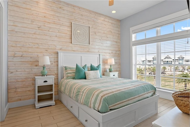 bedroom with wooden walls, light wood-type flooring, and a ceiling fan