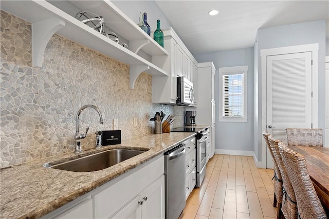 kitchen featuring light stone counters, open shelves, a sink, decorative backsplash, and appliances with stainless steel finishes