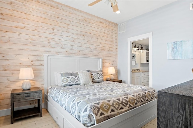 bedroom with wood walls, visible vents, ensuite bathroom, and light wood-type flooring