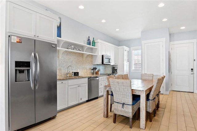 kitchen featuring a sink, open shelves, light stone counters, tasteful backsplash, and appliances with stainless steel finishes