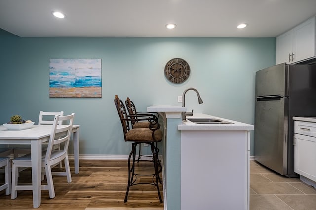 kitchen with white cabinetry, sink, stainless steel fridge, a kitchen breakfast bar, and a kitchen island with sink