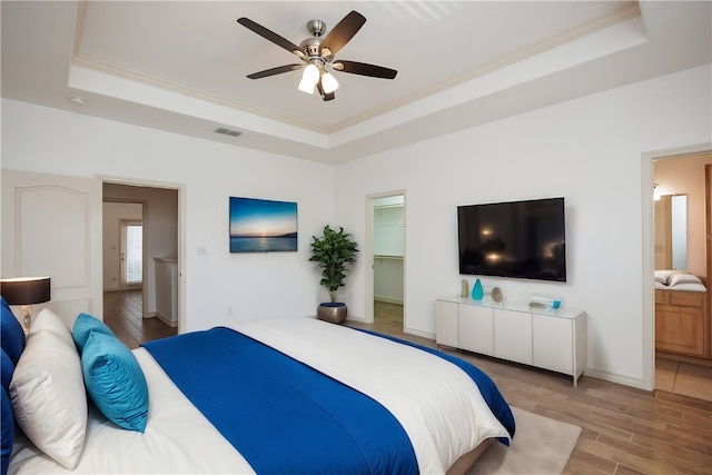 bedroom featuring a tray ceiling, a spacious closet, hardwood / wood-style flooring, and ensuite bath