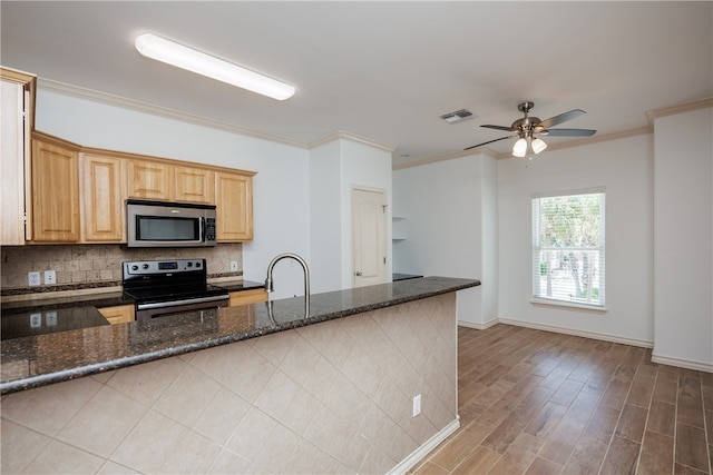 kitchen featuring kitchen peninsula, ornamental molding, dark stone counters, appliances with stainless steel finishes, and light wood-type flooring