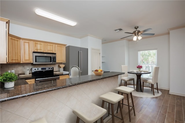 kitchen with a kitchen breakfast bar, appliances with stainless steel finishes, crown molding, and dark stone countertops