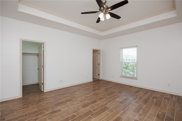 unfurnished bedroom featuring hardwood / wood-style flooring, ornamental molding, ceiling fan, a tray ceiling, and a walk in closet