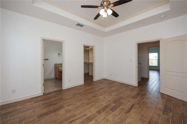 unfurnished bedroom with ceiling fan, dark hardwood / wood-style floors, a tray ceiling, a walk in closet, and a closet