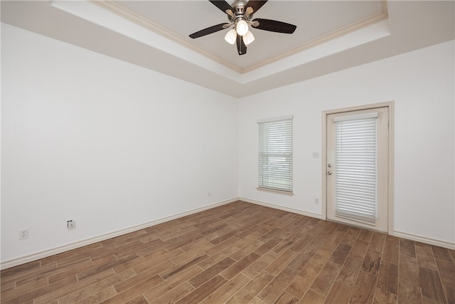 empty room with ceiling fan, dark hardwood / wood-style floors, ornamental molding, and a tray ceiling