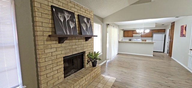 unfurnished living room featuring a textured ceiling, lofted ceiling, a notable chandelier, a brick fireplace, and light wood-type flooring