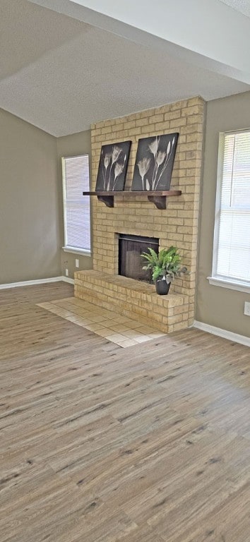 unfurnished living room featuring a brick fireplace, wood-type flooring, and a textured ceiling