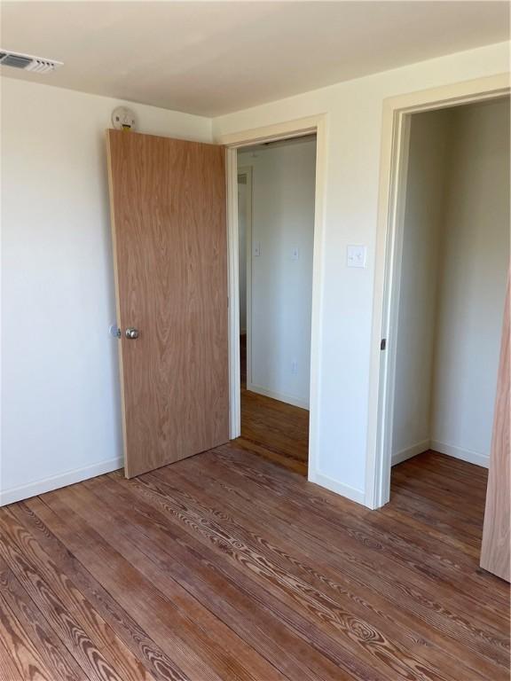 unfurnished bedroom featuring visible vents, baseboards, and wood finished floors