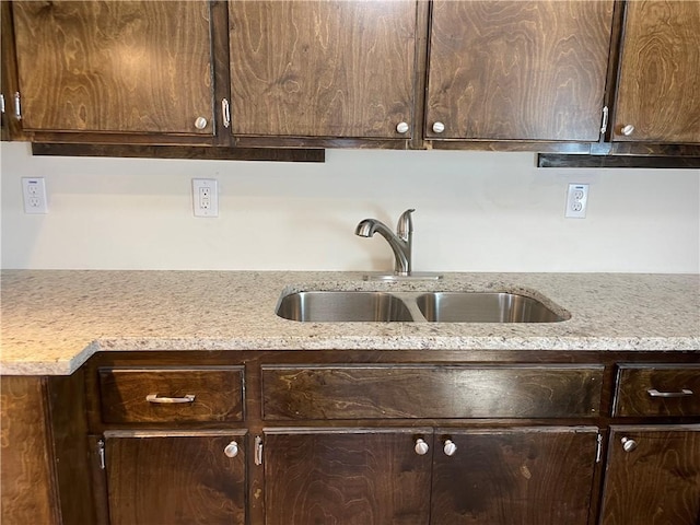 kitchen featuring light stone counters, dark brown cabinets, and a sink