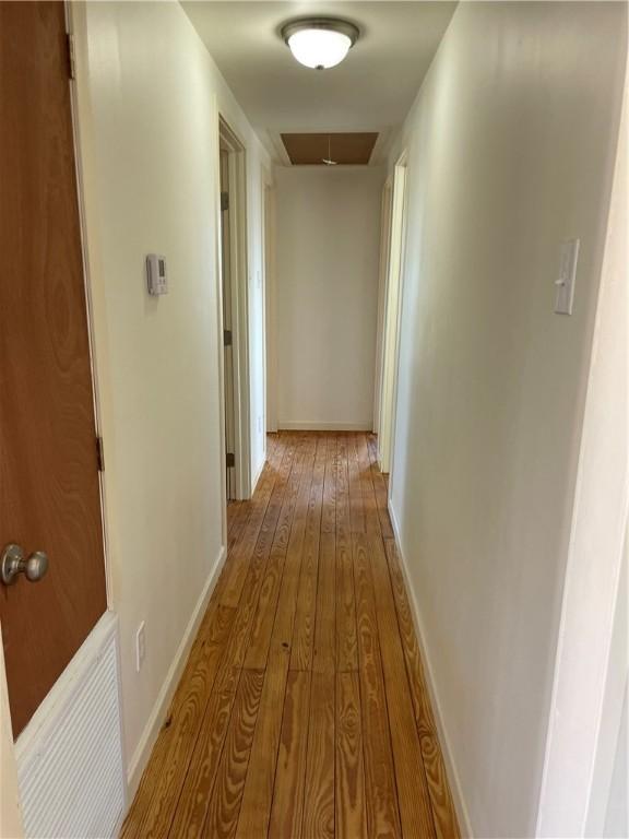 corridor with hardwood / wood-style flooring, attic access, and baseboards