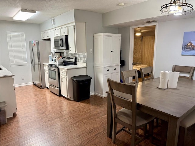 11614 Coleta Creek Dr, Corpus Christi, TX 78410 - kitchen featuring stainless steel appliances, wood finished floors, light countertops, white cabinetry, and decorative backsplash