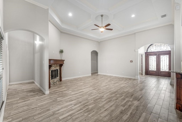 unfurnished living room with french doors, a stone fireplace, crown molding, light hardwood / wood-style flooring, and ceiling fan