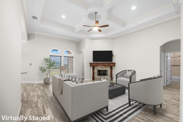 living room with ornamental molding, coffered ceiling, ceiling fan, light hardwood / wood-style floors, and a stone fireplace