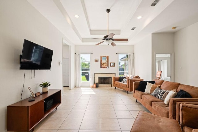 living room featuring light tile patterned floors, a fireplace, visible vents, a raised ceiling, and a ceiling fan