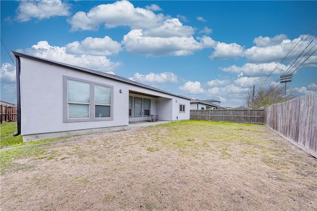 rear view of house featuring a yard, stucco siding, a patio, and a fenced backyard