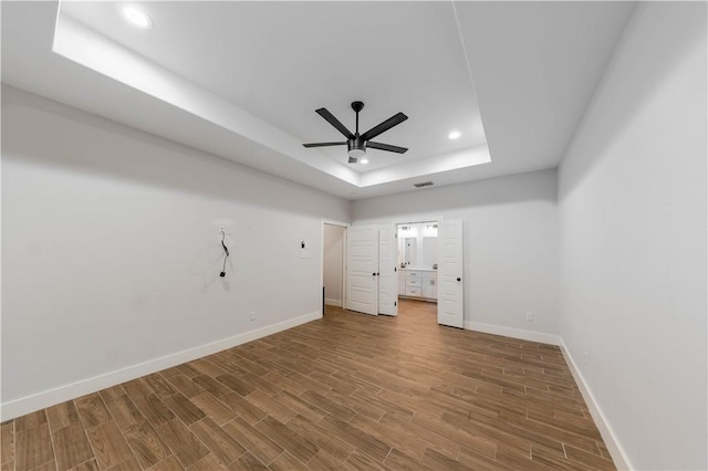 unfurnished bedroom with a raised ceiling, wood finished floors, and baseboards