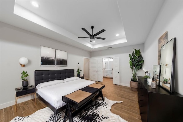 bedroom with a tray ceiling, recessed lighting, baseboards, and light wood-type flooring