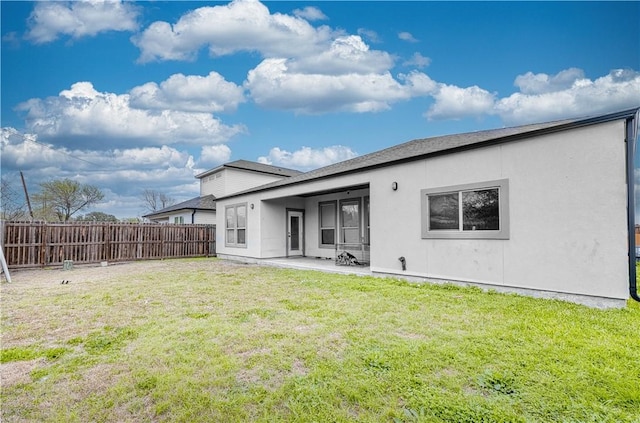 rear view of property with a patio area, a lawn, stucco siding, and fence