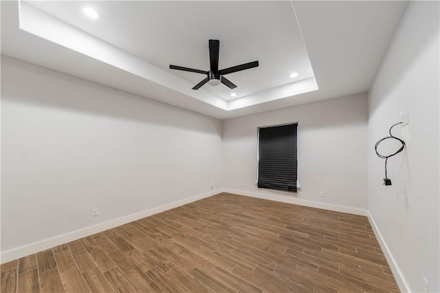 unfurnished room with a ceiling fan, a tray ceiling, wood finished floors, recessed lighting, and baseboards