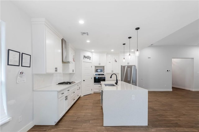 kitchen featuring visible vents, a sink, wood finished floors, stainless steel appliances, and wall chimney exhaust hood