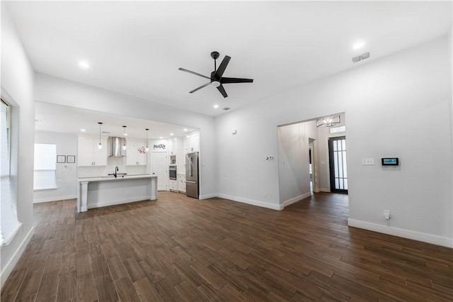 unfurnished living room with a sink, visible vents, baseboards, and dark wood-style flooring