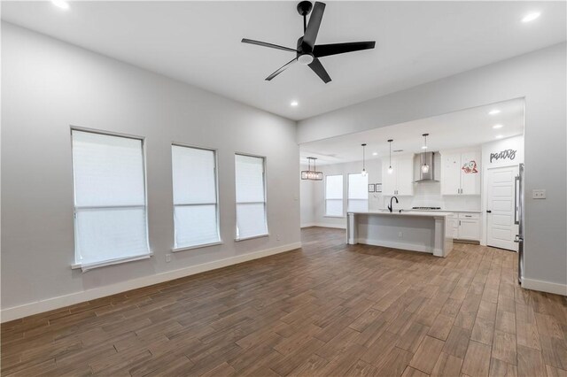 kitchen with a sink, open floor plan, wood finished floors, white cabinetry, and wall chimney exhaust hood