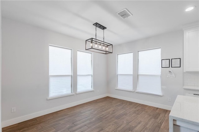 unfurnished dining area with visible vents, a healthy amount of sunlight, baseboards, and wood finished floors