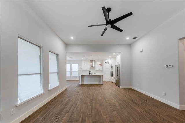 unfurnished living room with a sink, visible vents, baseboards, and dark wood-style flooring